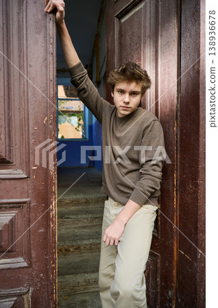 Teen leaning in doorway with gaze, intense eye contact, hand bracing doorframe, textured wood panels, warm interior behind, neutral sweater, confident model energy, cinematic color grading Teen leaning in doorway with gaze, intense eye contact, hand bracing doorframe, textured wood panels, warm interior behind, neutral sweater, confident model energy, cinematic color grading 138936678