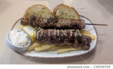 Pork skewer and lamb skewer served on the fries with tzatziki and bread on the side 138936709