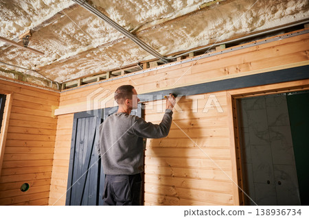 Man installing and aligning sliding door rail on wooden wall, checking position with hand. Interior construction work, home renovation, carpentry installation and modern design concept 138936734