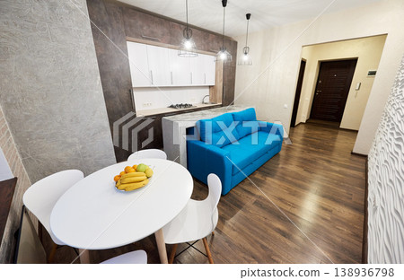 Modern studio apartment with blue sofa, dining table and compact kitchen in open plan interior. Stylish home design with wooden floor, pendant lights and urban living concept 138936798
