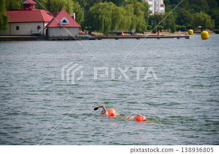 Two swimmers training freestyle in open water near lakeside town, using safety buoys in choppy conditions. Concept of triathlon, endurance and outdoor sport Two swimmers training freestyle in open water near lakeside town, using safety buoys in choppy conditions. Concept of triathlon, endurance and outdoor sport 138936805
