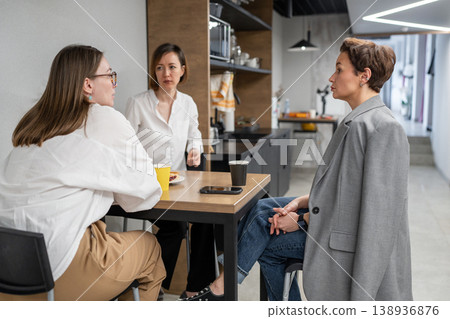 Team members in kitchen seated at counter having conversation and lunch during company meal break. Conversation, lunch, kitchen, office, teamwork, team. Team members in kitchen seated at counter having conversation and lunch during company meal break. Conversation, lunch, kitchen, office, teamwork, team. 138936876
