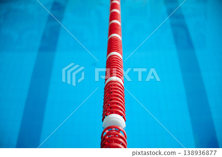 Swimming pool lane divider in sharp focus. Red and white lane line centered over blue water with shallow depth of field, minimal sport background 138936877