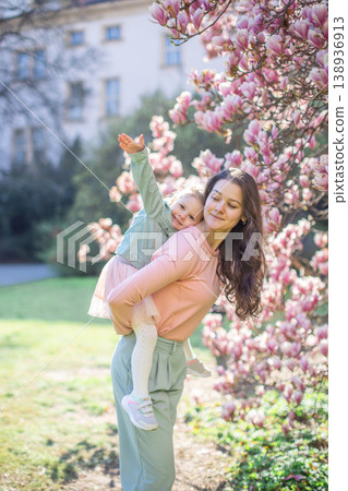 Trendy mom with her little daughter under blooming magnolia trees in a Prague park. Capturing a stylish family moment with a modern approach to parenting Trendy mom with her little daughter under blooming magnolia trees in a Prague park. Capturing a stylish family moment with a modern approach to parenting 138936913