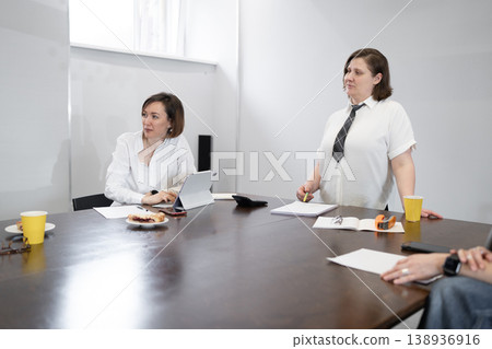 Smiling woman talking to colleague during breakfast business meeting at long table in modern office. Smiling, meeting, breakfast, woman, business. 138936916