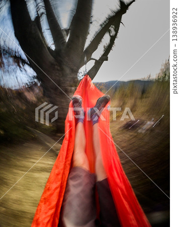 POV relaxing in hammock outdoors, motion blur effect showing swinging movement, legs view under tree in countryside with bright sky and nature landscape 138936922