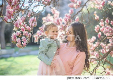 Trendy mom with her little daughter under blooming magnolia trees in a Prague park. Capturing a stylish family moment with a modern approach to parenting 138936929