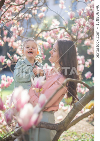 Trendy mom with her little daughter under blooming magnolia trees in a Prague park. Capturing a stylish family moment with a modern approach to parenting Trendy mom with her little daughter under blooming magnolia trees in a Prague park. Capturing a stylish family moment with a modern approach to parenting 138936946
