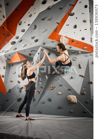 Woman gives high five to climbing partner on bouldering wall in gym. Image for teamwork, success, support, friendship, fitness club promotion 138936973