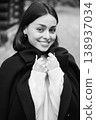 Smiling young woman holding coat collar in black and white portrait, wearing soft knitwear and looking at camera. Ideal for fashion, comfort, timeless style, and advertising 138937034