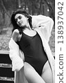 Elegant woman in swimsuit and bathrobe relaxing on terrace, holding champagne glass. Black and white portrait conveying luxury, wellness lifestyle, calm mood and refined leisure 138937042