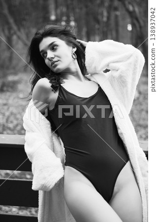 Elegant woman in swimsuit and bathrobe relaxing on terrace, holding champagne glass. Black and white portrait conveying luxury, wellness lifestyle, calm mood and refined leisure 138937042
