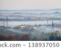 Fog drifts over suburban houses and autumn forest in layered morning landscape with power lines. Suitable for weather, environment, energy infrastructure, rural living or seasonal themes 138937050
