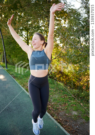 Woman raising arms and celebrating after run. Happy female in sportswear on park path, outdoor fitness, success, achievement, active lifestyle, energy and motivation concept Woman raising arms and celebrating after run. Happy female in sportswear on park path, outdoor fitness, success, achievement, active lifestyle, energy and motivation concept 138937055