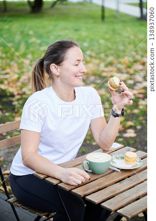 Woman savoring dessert at street cafe table. Female athlete in sportswear enjoying coffee break after exercise, indulgence, relaxation, lifestyle balance and reward concept Woman savoring dessert at street cafe table. Female athlete in sportswear enjoying coffee break after exercise, indulgence, relaxation, lifestyle balance and reward concept 138937060