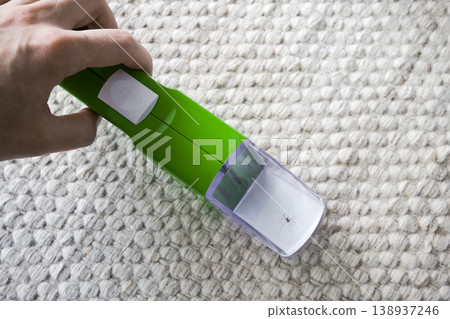 A close up of a hand holding a green insect and spider catcher with a spider inside, against a textured carpet background. A close up of a hand holding a green insect and spider catcher with a spider inside, against a textured carpet background. 138937246