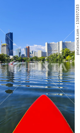 Red paddleboard on water with modern city skyline reflection. Summer water sport, mental vitality, burst of energy. 138937283
