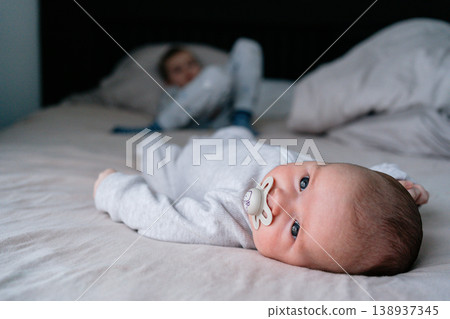 Older child lying next to newborn baby on bed at home. Family bonding, sibling love, early childhood and parenting concept in soft natural light interior 138937345
