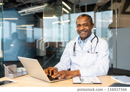 Mature medical professional, a smiling male doctor, working on a laptop at his desk in a modern healthcare office, providing telehealth and digital patient care Mature medical professional, a smiling male doctor, working on a laptop at his desk in a modern healthcare office, providing telehealth and digital patient care 138937366