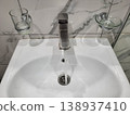 Water flows from the tap in the bathroom, where there is a white handwashing sink with glass accessories 138937410