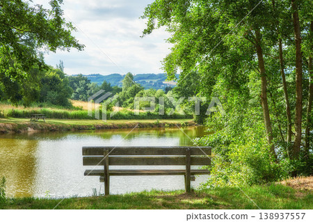 Relaxing nature view of a park bench with trees, grass, and a lake in the background. A forest and field landscape in the countryside. Natural outdoor setting perfect for a summer day outside 138937557