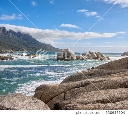 A calming ocean view of the rocky coast of Camps Bay in Cape Town, South Africa. Boulders at a beach with the tide and current coming in and Table Mountain on the horizon. Tidal waves washing ashore A calming ocean view of the rocky coast of Camps Bay in Cape Town, South Africa. Boulders at a beach with the tide and current coming in and Table Mountain on the horizon. Tidal waves washing ashore 138937604
