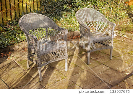 Woven armchairs outside in a rustic garden with green plants for relaxing after gardening. Yard landscape with two wooden chairs in nature in a backyard patio to enjoy the sun on a warm winter day 138937675
