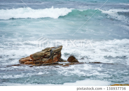 One rock with waves crashing around it. Rock formation in calm peaceful blue ocean. Waves moving in and out by the seaside. Rocky shoreline with clear water. Holiday location for travel destination One rock with waves crashing around it. Rock formation in calm peaceful blue ocean. Waves moving in and out by the seaside. Rocky shoreline with clear water. Holiday location for travel destination 138937736