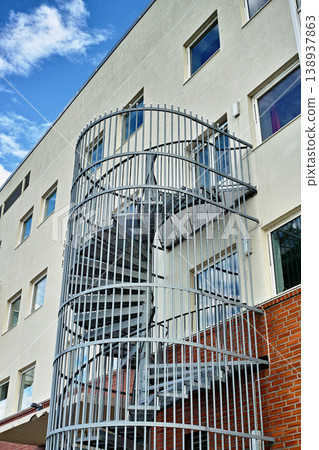 A spiral staircase running down the side of a building. Emergency exit fire escape. Backyard escape stairs. Caged emergency ladder for the safety of the residents in case of a fire or fire drill 138937863