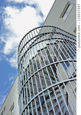 A spiral staircase on the outside of a building. Grey steel spiral stairs built on the side of modern industrial office building. Low angle of a metal circular fire escape staircase with railings 138937897