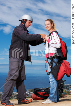 Man, woman and ready with safety for paragliding, extreme sport and helping by ocean in sunshine. Coaching, fitness and adventure with helmet, backpack and parachute for jump, outdoor and blue sky Man, woman and ready with safety for paragliding, extreme sport and helping by ocean in sunshine. Coaching, fitness and adventure with helmet, backpack and parachute for jump, outdoor and blue sky 138937924