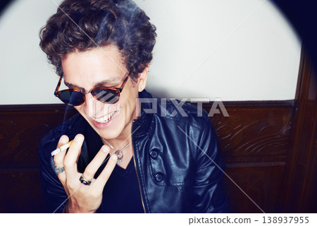 Man with cigarette, rock fashion and smile with rockstar attitude on white background in spotlight. Cool punk style, grunge and smoking, confident and happy male model in studio with sunglasses. 138937955