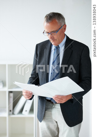 Businessman, standing amd reading documents in office or company contract, report information or confidential file. Male person, suit or paperwork thinking or corporate agreement, decision or folder 138938043
