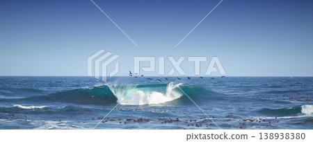 One wave crashing in the sea with seagulls flying and copy space. Rolling waves in a calm peaceful ocean against a blue clear sky. Calm and serene nature scene. Waves by the seaside on a shoreline One wave crashing in the sea with seagulls flying and copy space. Rolling waves in a calm peaceful ocean against a blue clear sky. Calm and serene nature scene. Waves by the seaside on a shoreline 138938380