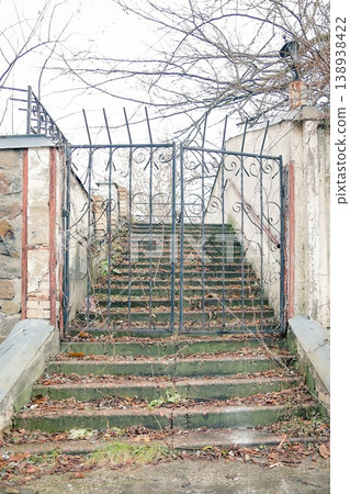 Old wrought iron gate covered with black paint and rust, leading to the old staircase up along the wall, with a reinforced table on it Old wrought iron gate covered with black paint and rust, leading to the old staircase up along the wall, with a reinforced table on it 138938422