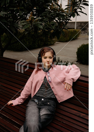 teenager listens to music while sitting on bench in outdoor setting during daytime teenager listens to music while sitting on bench in outdoor setting during daytime 138938889