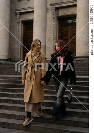 Mother and teenage daughter walk hand in hand down steps in a city setting on a sunny day 138938902