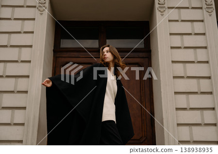 Girl walks outside a building wearing a black cape in an urban setting during daytime Girl walks outside a building wearing a black cape in an urban setting during daytime 138938935