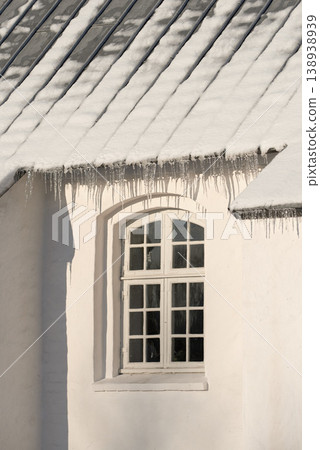 Empty building with ice damming on the roof on a cold winter day. The exterior of a home or house with snow on the rooftop on a sunny afternoon. Frost on a historic church in a village Empty building with ice damming on the roof on a cold winter day. The exterior of a home or house with snow on the rooftop on a sunny afternoon. Frost on a historic church in a village 138938939