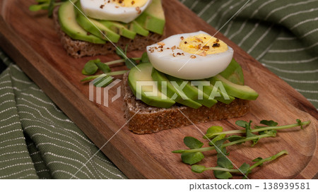 Pair of healthy avocado toasts with eggs and microgreens on a rustic wooden board 138939581