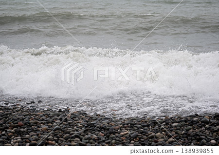 Waves crashing on rocky shore with pebbles and foamy water in coastal landscape Waves crashing on rocky shore with pebbles and foamy water in coastal landscape 138939855
