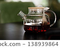 Glass teapot with wooden lid and tea bag on black table in modern interior setting 138939864