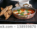 Shakshuka dish with poached eggs, tomatoes, and herbs served with toasted bread on slate board 138939870