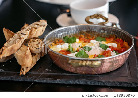 Shakshuka dish with poached eggs, tomatoes, and herbs served with toasted bread on slate board Shakshuka dish with poached eggs, tomatoes, and herbs served with toasted bread on slate board 138939870