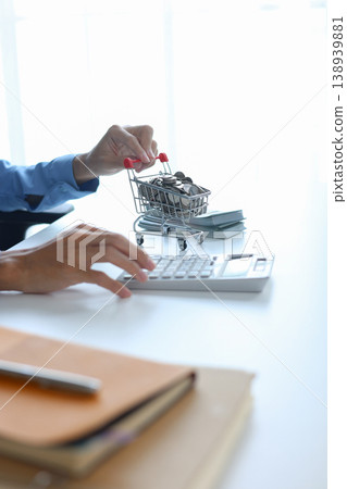 Businessman calculating online shopping expenses and saving with shopping cart filled with coins and stack of crash on white table 138939881
