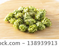Dried hop cones are placed on a wooden table, conveying the aroma and bitterness of hops used as an ingredient in beer brewing. 138939913