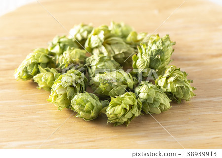 Dried hop cones are placed on a wooden table, conveying the aroma and bitterness of hops used as an ingredient in beer brewing. 138939913