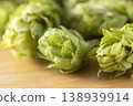 Dried hop cones are placed on a wooden table, conveying the aroma and bitterness of hops used as an ingredient in beer brewing. 138939914