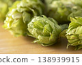 Dried hop cones are placed on a wooden table, conveying the aroma and bitterness of hops used as an ingredient in beer brewing. 138939915