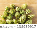 Dried hop cones are placed on a wooden table, conveying the aroma and bitterness of hops used as an ingredient in beer brewing. 138939917